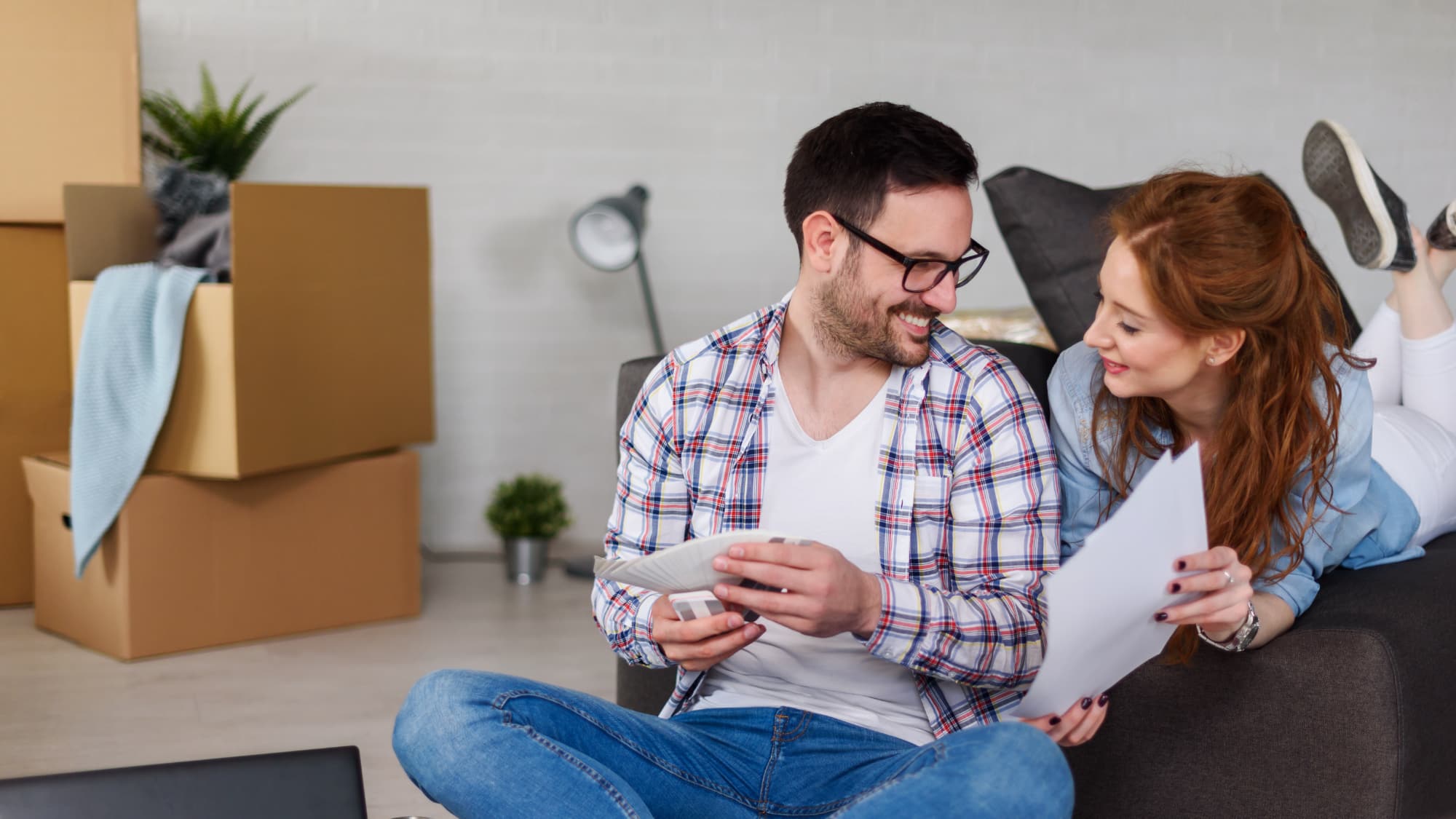 young couple smiling at each other while sitting on the floor of their new home surrounded by boxes