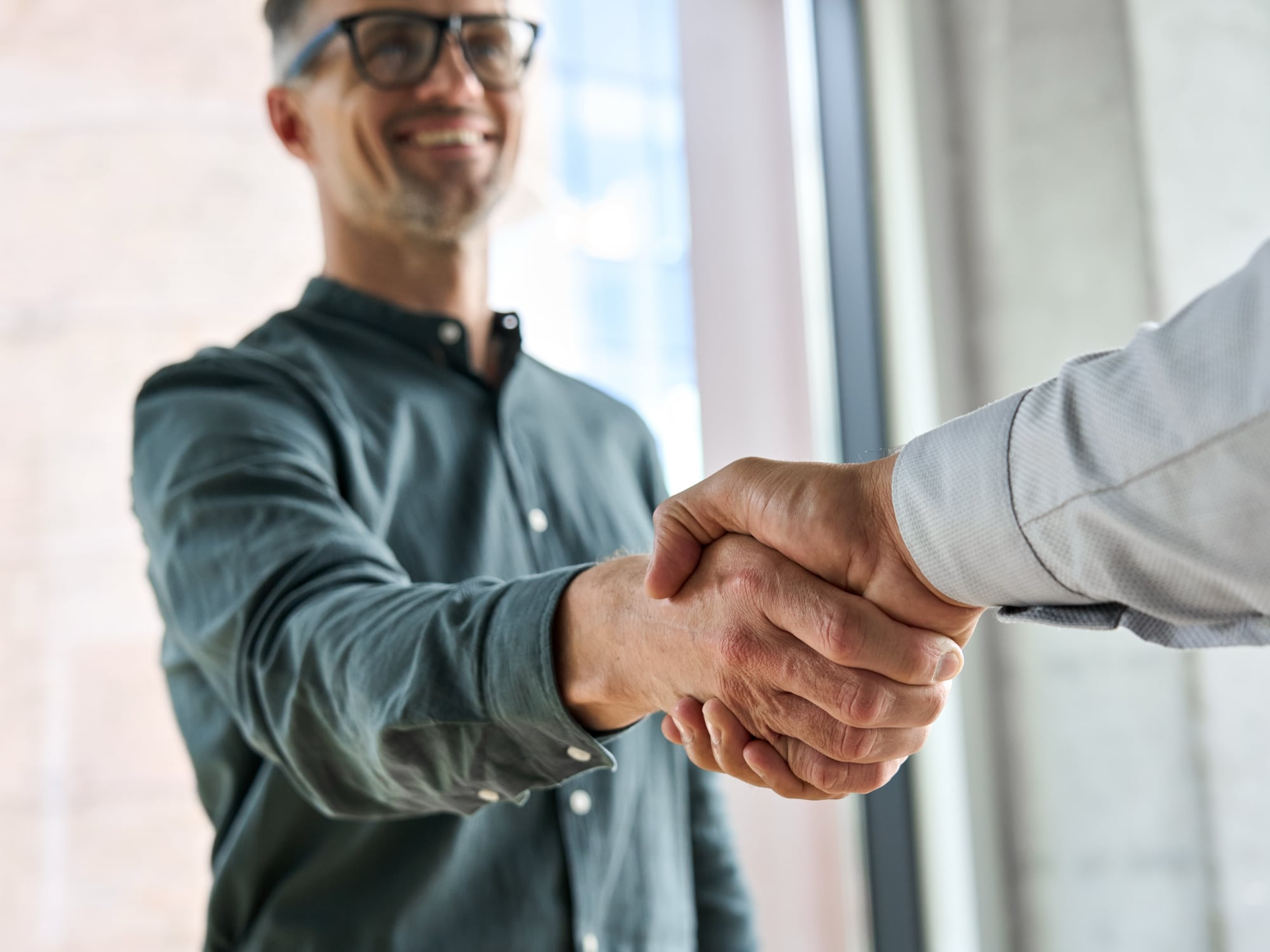 A middle aged man wearing glasses and a green button shirt shaking hands with a real estate agent