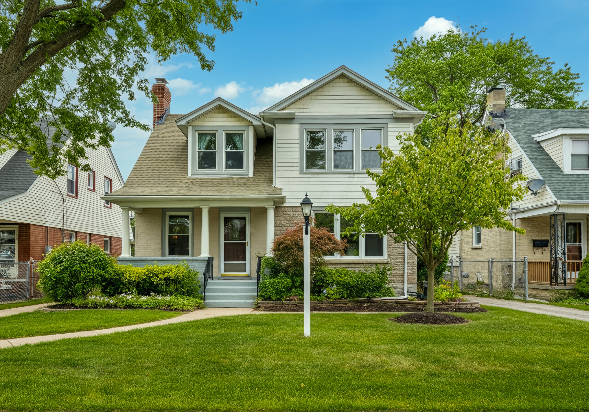 A brick 1940's two story home with a small tree in the yard in Plymouth Michigan