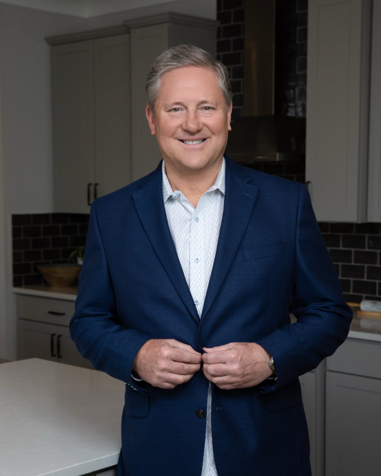 Todd Taliaferro, standing in a modern kitchen wearing a blue suit smiling at the camera